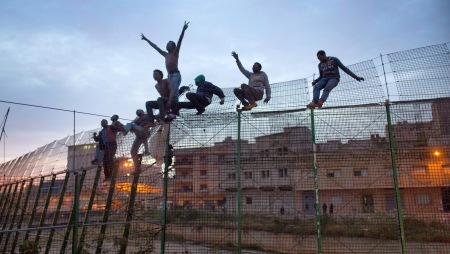 A triumphant migrant’s work is almost done as he reaches the top of the present 6m fence between Morocco and Spain at Melilla