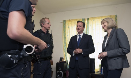 A smiling David Cameron and Theresa May speak with altogether less camera aware officers, following the raid in Slough 